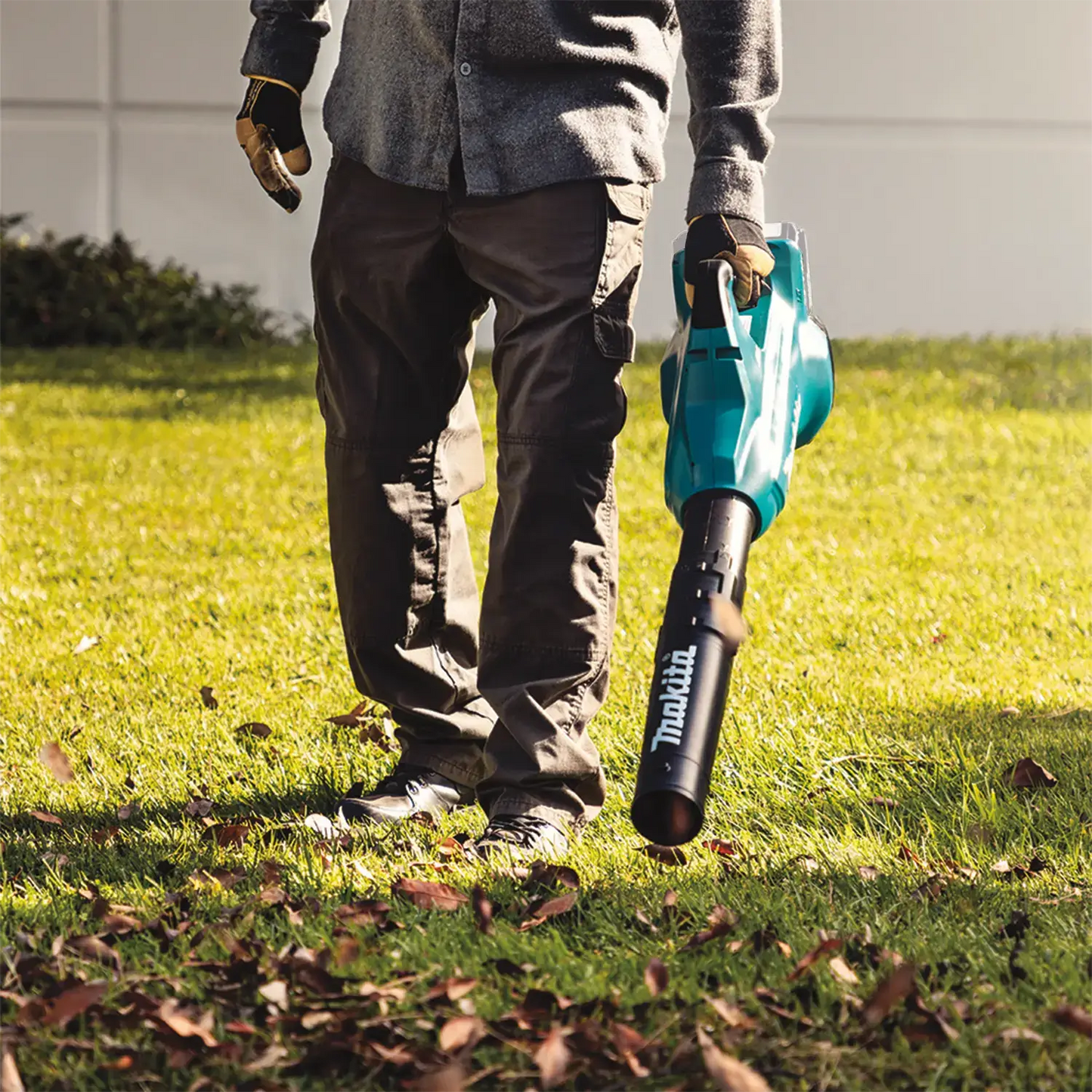 Person holding a Makita leaf blower on a grassy area with scattered leaves.