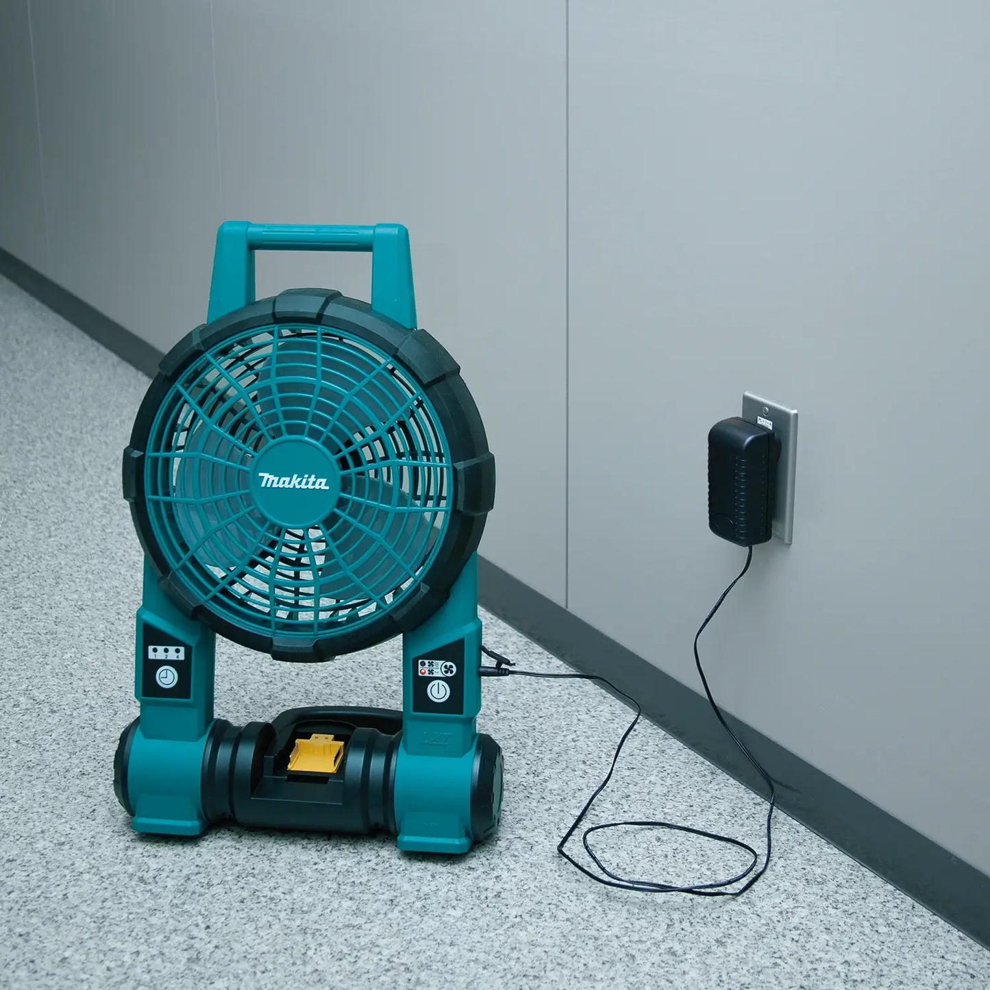 Makita portable fan plugged into an outlet on a concrete floor.