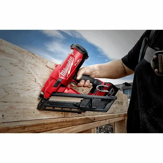 Person using a Milwaukee nail gun on a wooden surface with a blue sky in the background