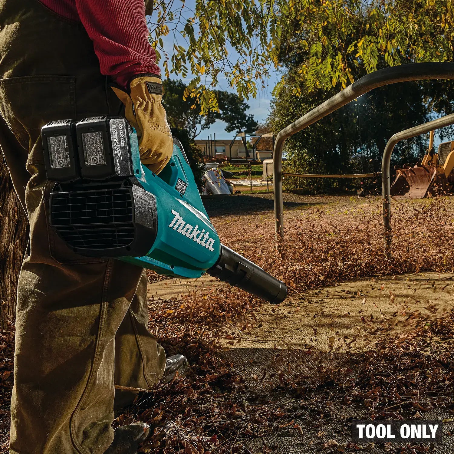 Person using a Makita leaf blower in an outdoor setting with trees and a fence in the background.