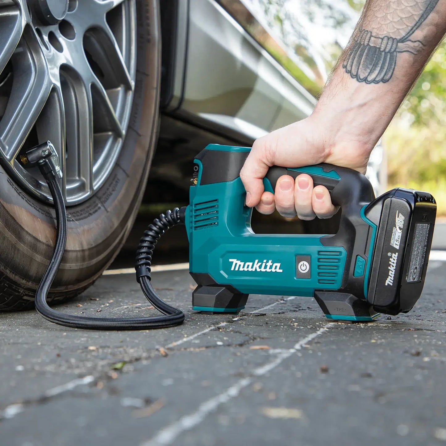 Person using a Makita tire inflator on a car tire outdoors.