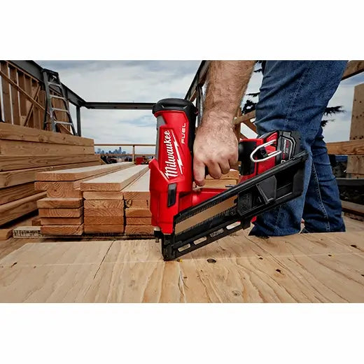 Person using a Milwaukee nail gun on a construction site with wooden planks in the background.