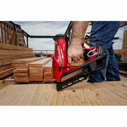 Person using a Milwaukee nail gun on a construction site with wooden planks in the background.