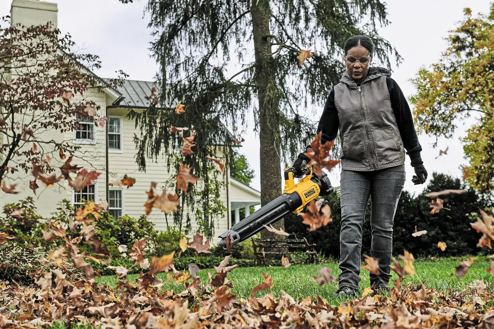 Person using a leaf blower to clear leaves from a lawn in front of a house.