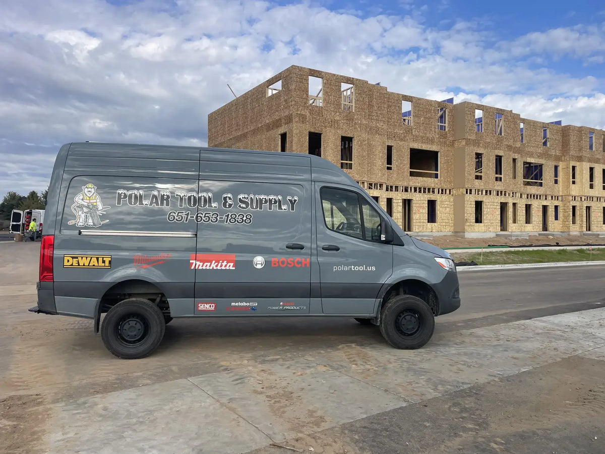 A gray commercial van parked outdoors in front of an unfinished wood building under a blue sky. The side of the van is branded with 'POLAR TOOL & SUPPLY' and includes logos for DeWalt, Makita, and Bosch.