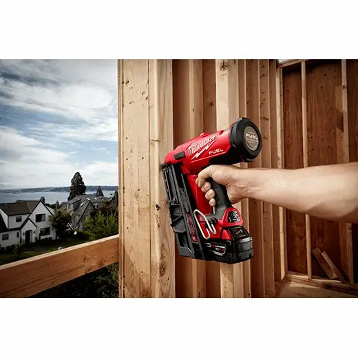 Person holding a red Milwaukee power tool against a wooden construction background with a scenic view.
