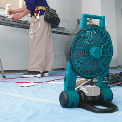 Teal and black portable fan on a blue floor with a person in the background.
