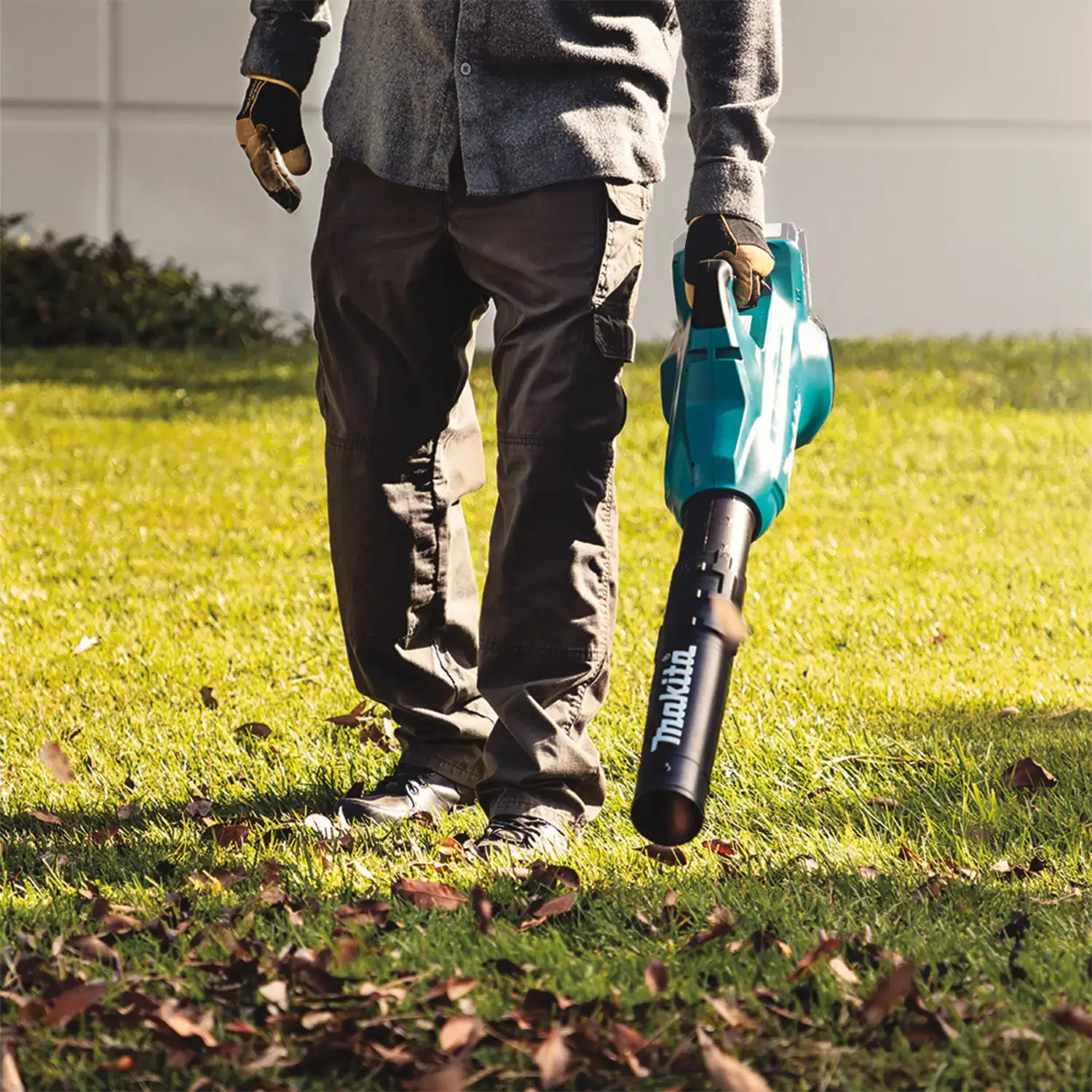 Person holding a Makita leaf blower on a grassy area with scattered leaves.