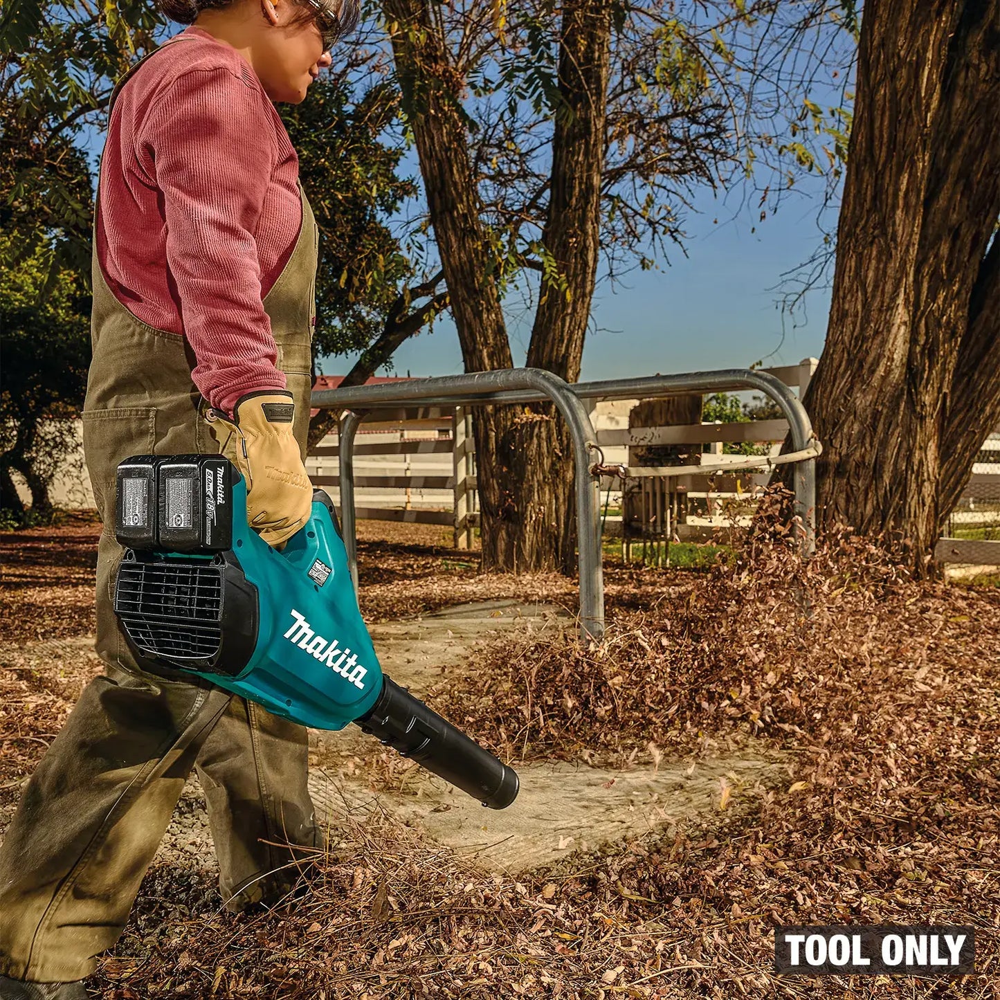 Person using a Makita leaf blower in an outdoor setting with trees and a fence.