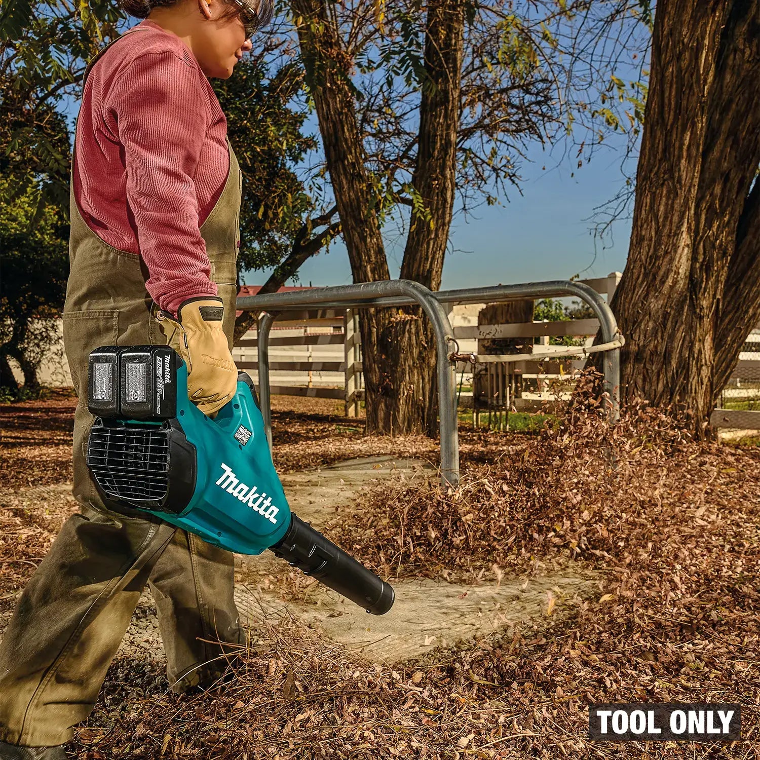 Person using a Makita leaf blower in an outdoor setting with trees and a fence.