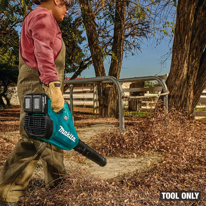 Person using a Makita leaf blower in an outdoor setting with trees and a fence.