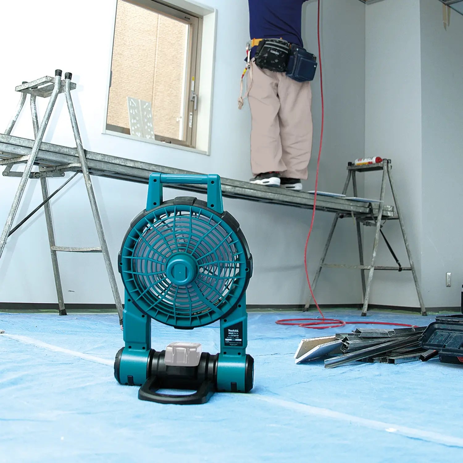 Blue portable fan on a blue floor with a person working in the background.
